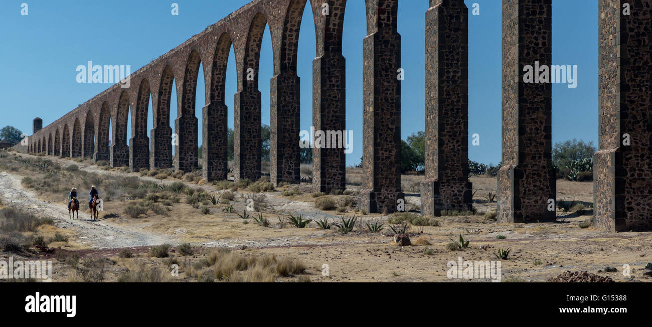 2 Mexican cowboys riding horses next to Aqueduct Acueducto de Tembleque which spans 45 Km  between Hidalgo and Mexico States. Stock Photo