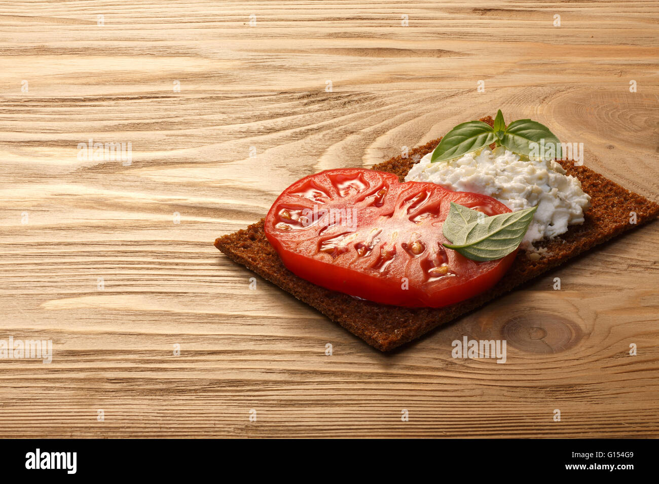 Bread crisp (crispbread open-faced sandwich) with heirloom tomato, cream cheese and fresh basil leaves on wooden table. Infinite Stock Photo