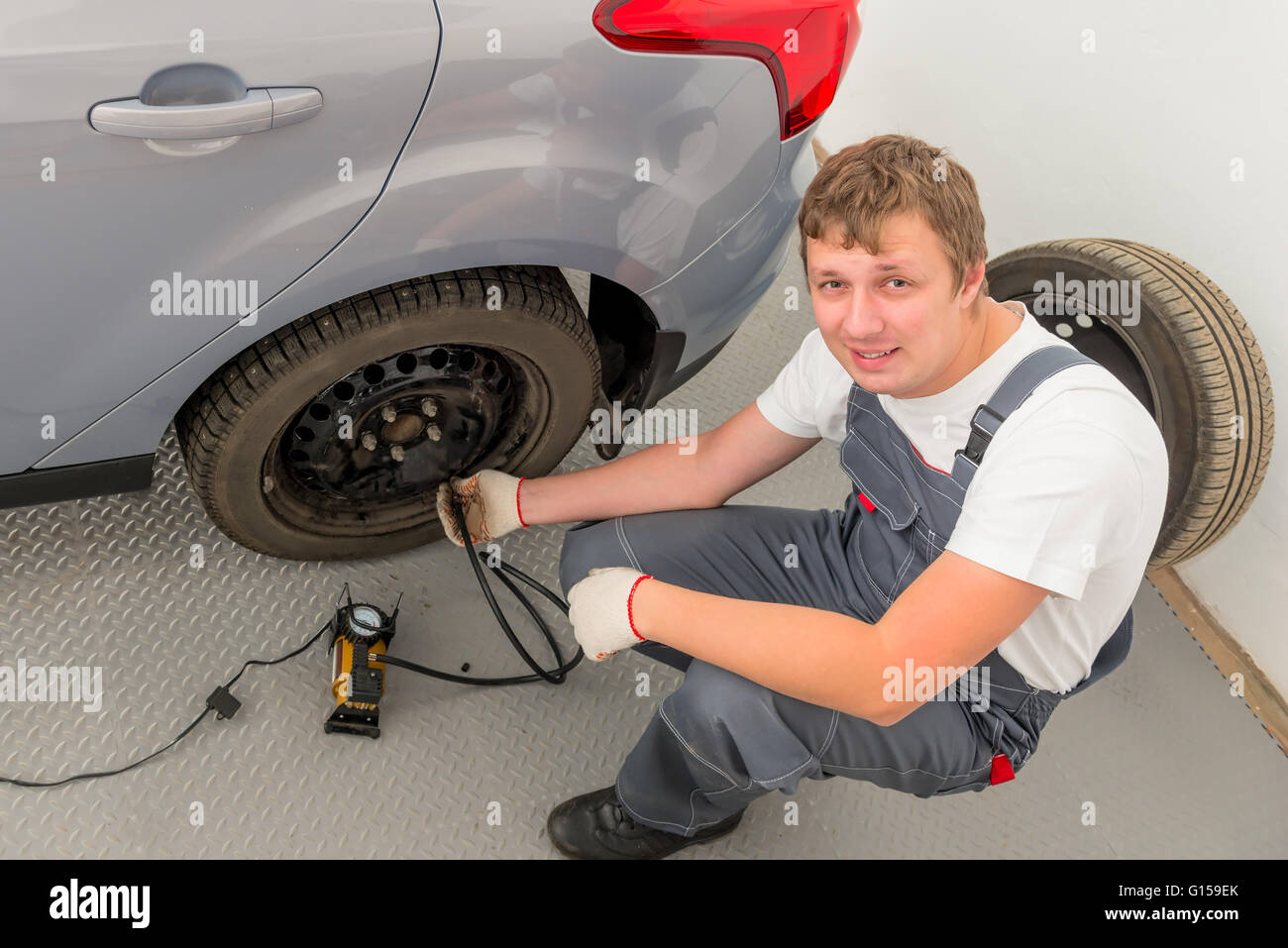 smiling mechanic a pump inflates the the wheel in garage Stock Photo ...