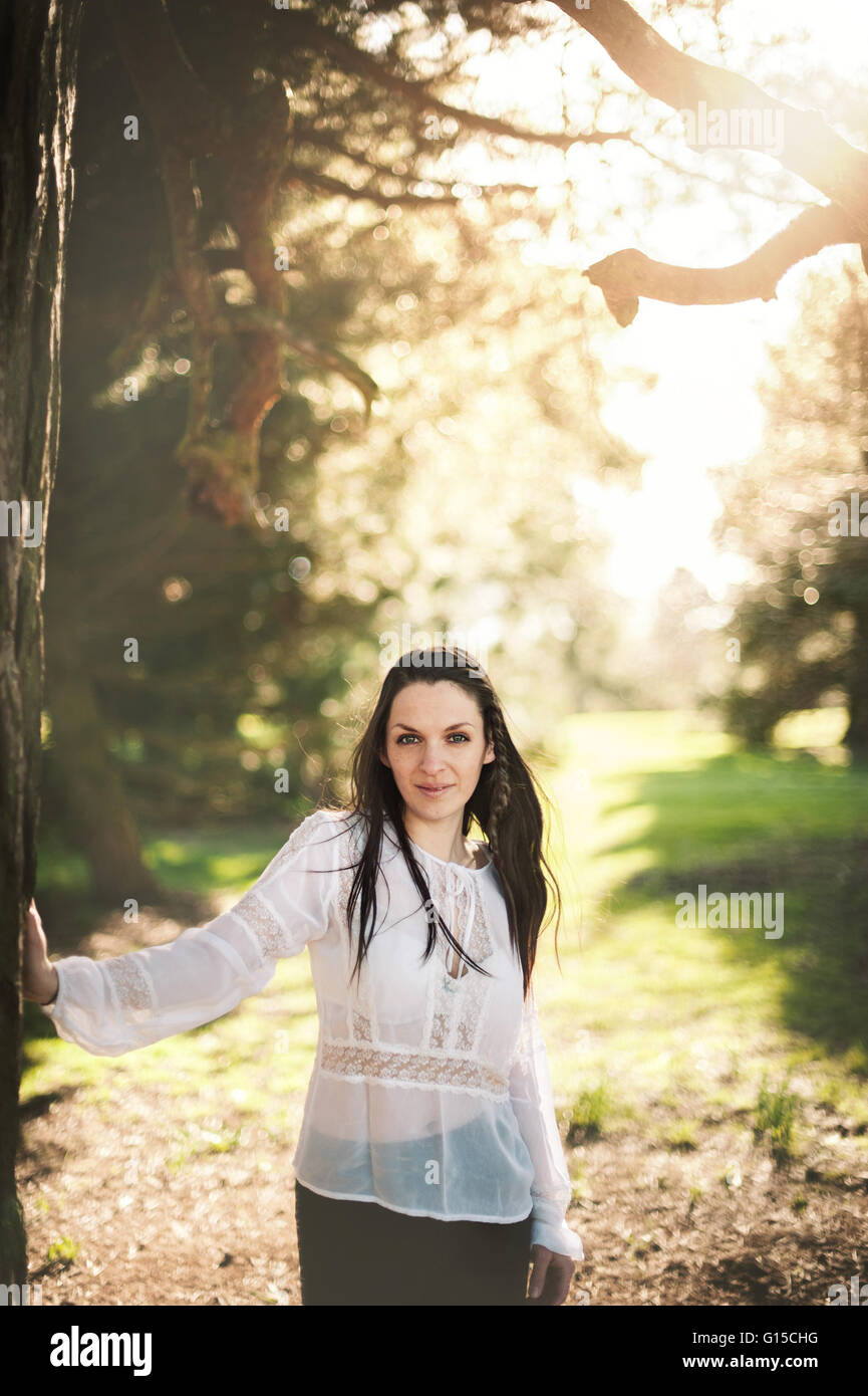 beautiful dark hair woman standing and touching tree Stock Photo