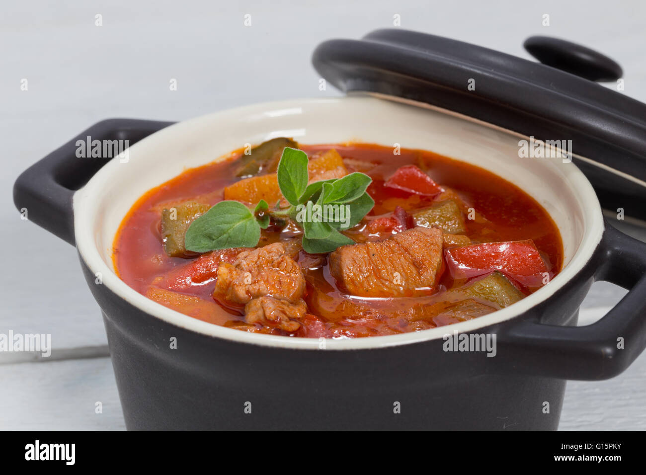 Goulash in a black cocotte with marjoram on white wood. Stock Photo