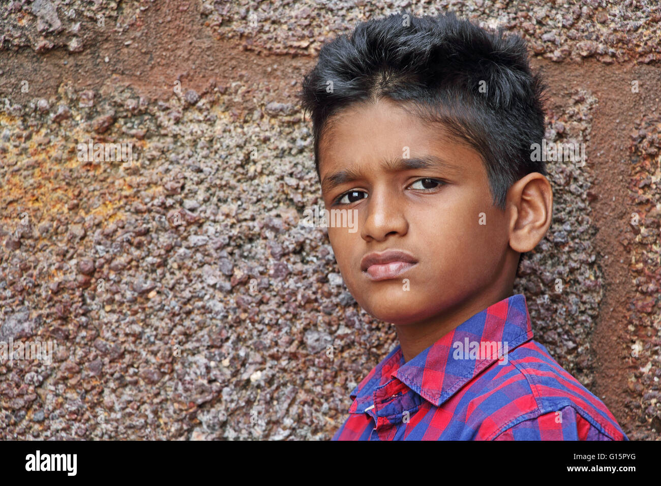 Teenage boy in angry and upset mood, red brick wall background Stock Photo