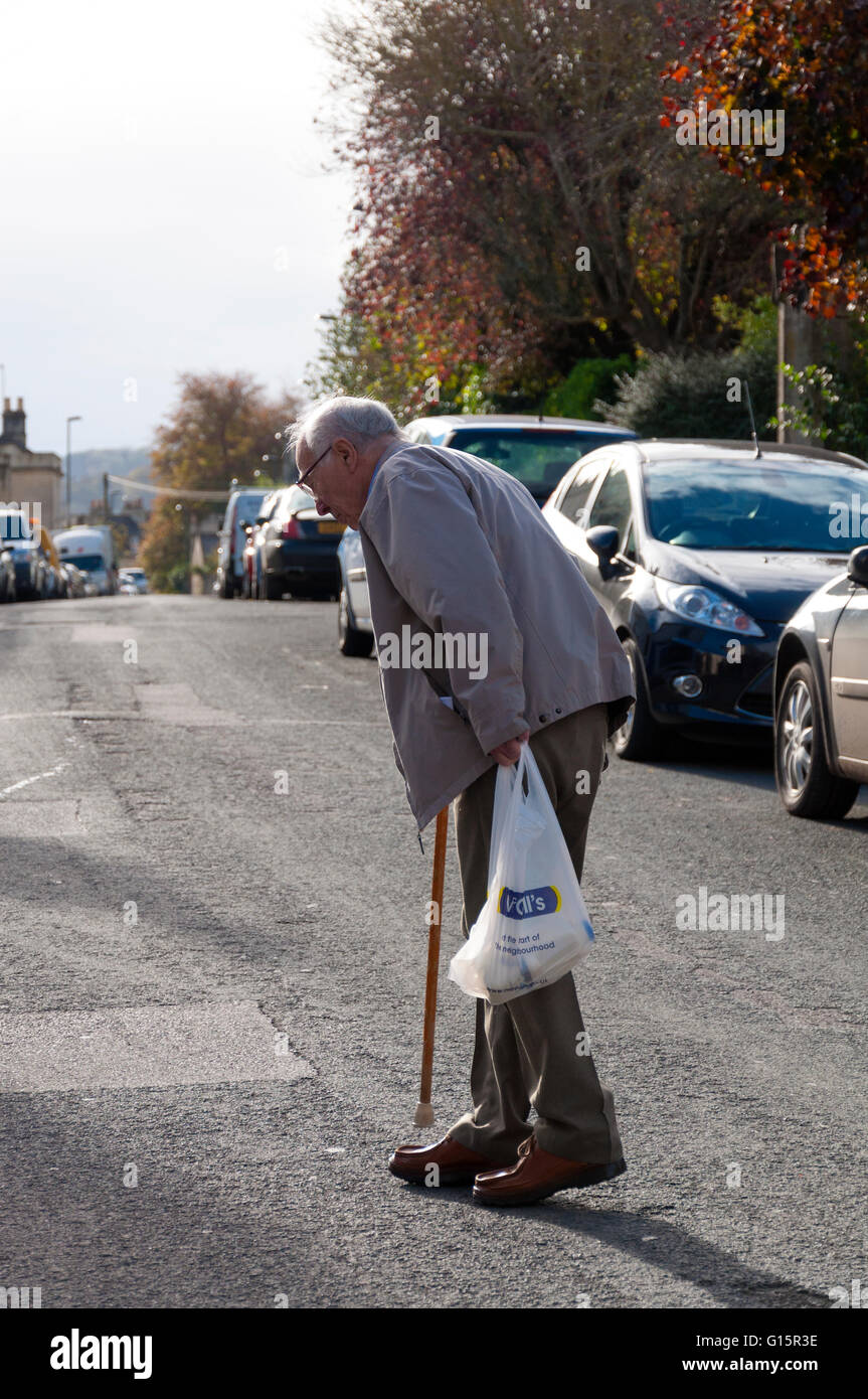 Elderly senior man crossing the road with shopping bag and walking stick Stock Photo
