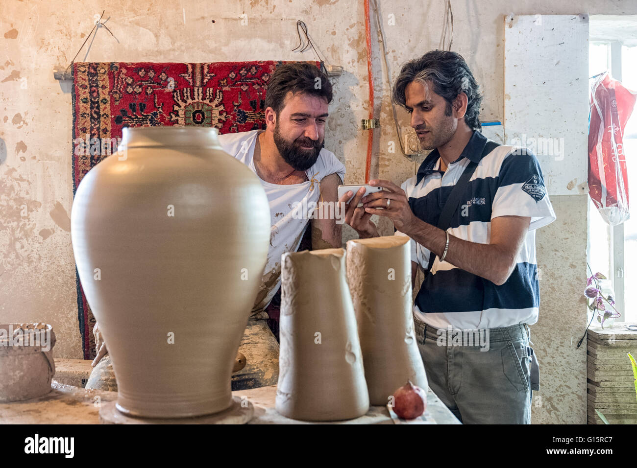 Hossein using his cell phone to show Iradj Naderi marketing ideas for his pottery in his workshop in Lalejin, Hamadan Province, Iran. Stock Photo