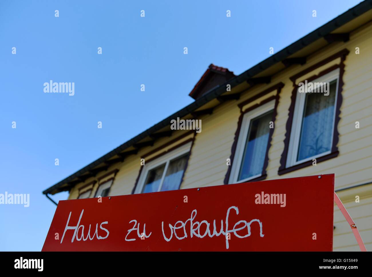 A sign that says "Haus zu verkaufen" (german, house for sale) stands in front of a house