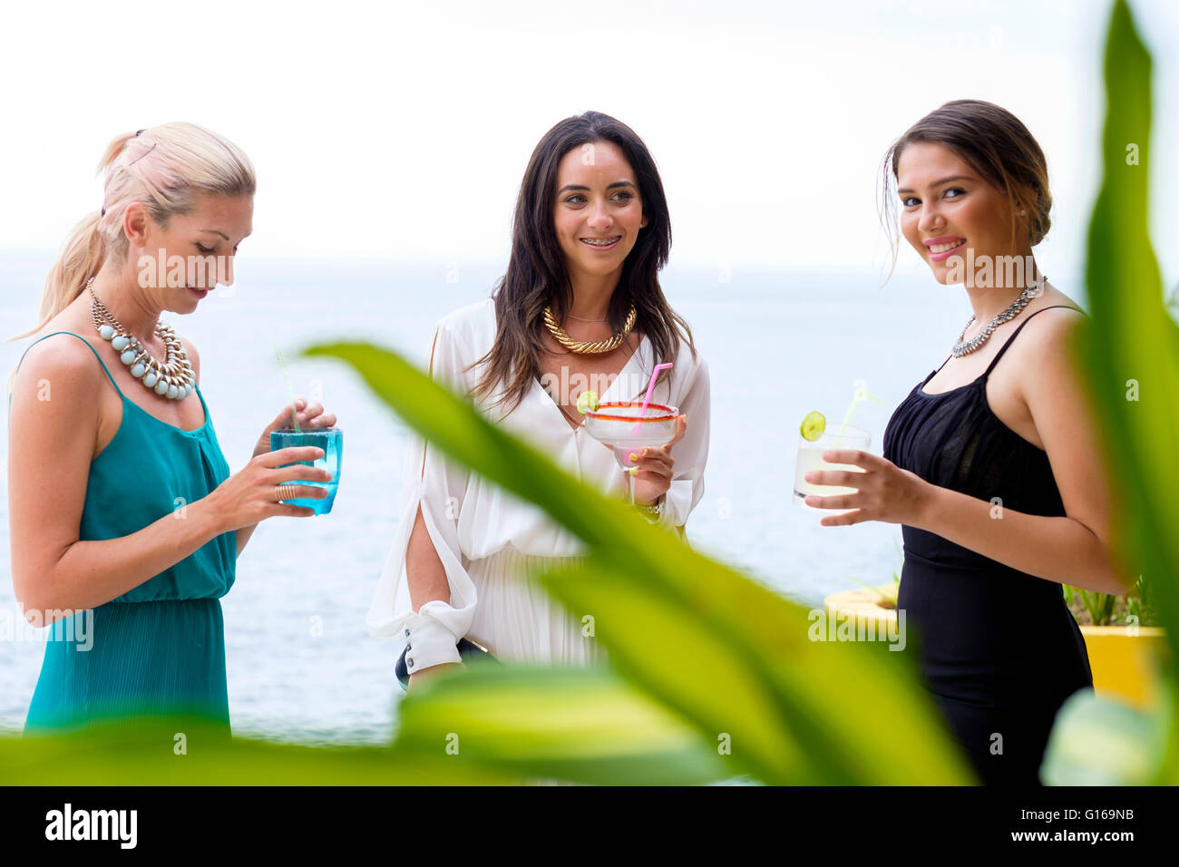 Three young attractive women in elegant dresses enjoying an outdoor cocktail party in Puerto Vallarta, Mexico Stock Photo