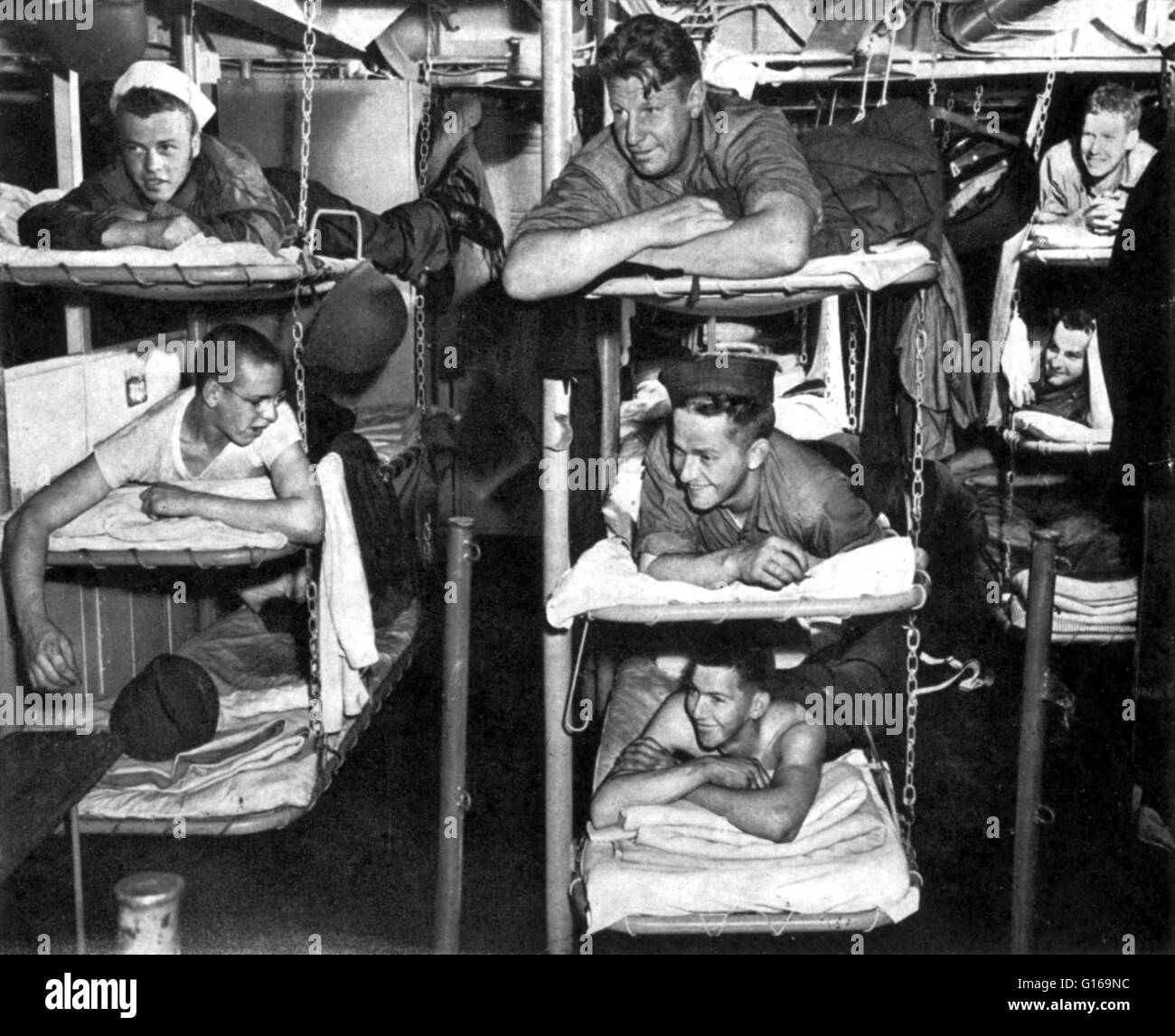Sailors 'at home' in crew quarters of ship bound for North Africa on the way to invade Sicily during World War II, July 1943. Triple deck bunks fold up during daytime to make room for mess tables and recreation. Soldiers live in narrow compartments on eit Stock Photo
