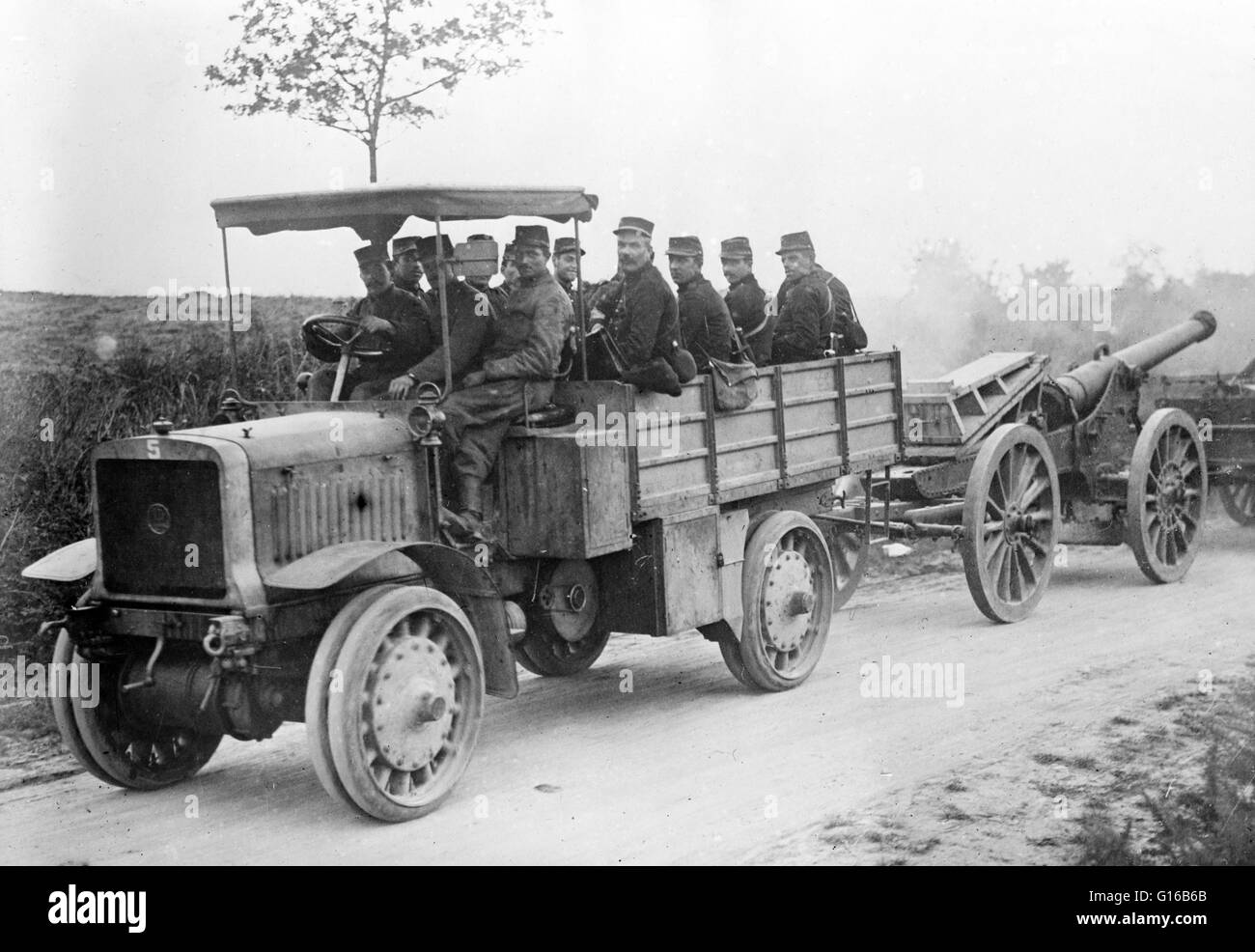 French soldiers in motor tractor which is pulling a large gun along the road at the beginning of World War I. Siege artillery were heavy guns and other bombardment devices designed to bombard fortifications, cities, and other fixed targets. They were capa Stock Photo