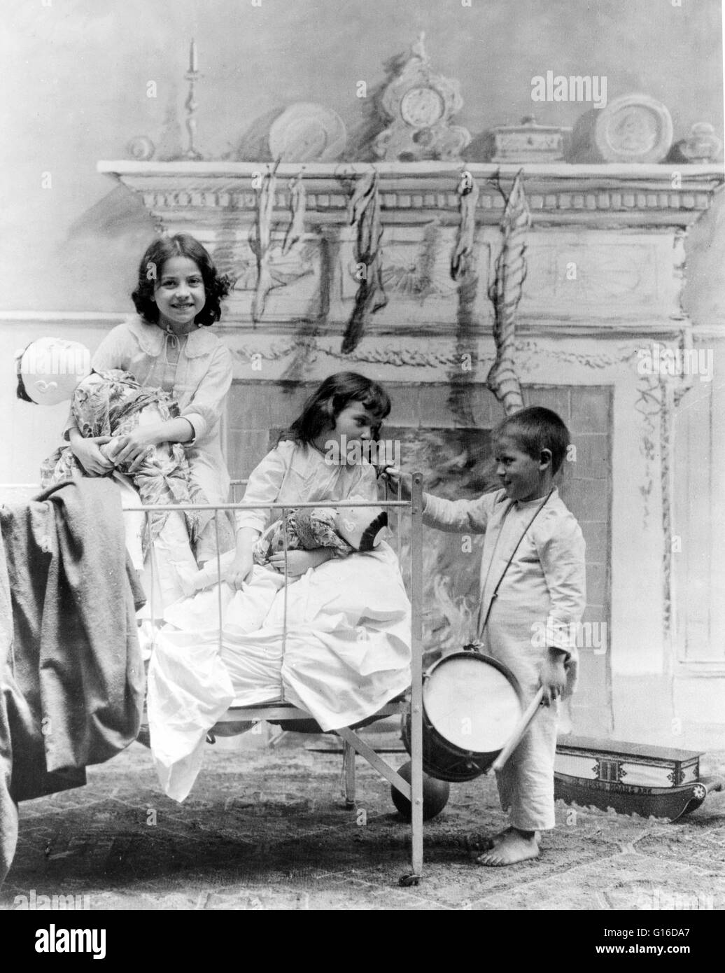 Entitled: 'Christmas morning' showing two girls in bed, playing with Japanese dolls, and a boy with a drum stands at the bedside. Stockings hang from the mantel behind them. Christmas is an annual commemoration of the birth of Jesus Christ and a widely ob Stock Photo