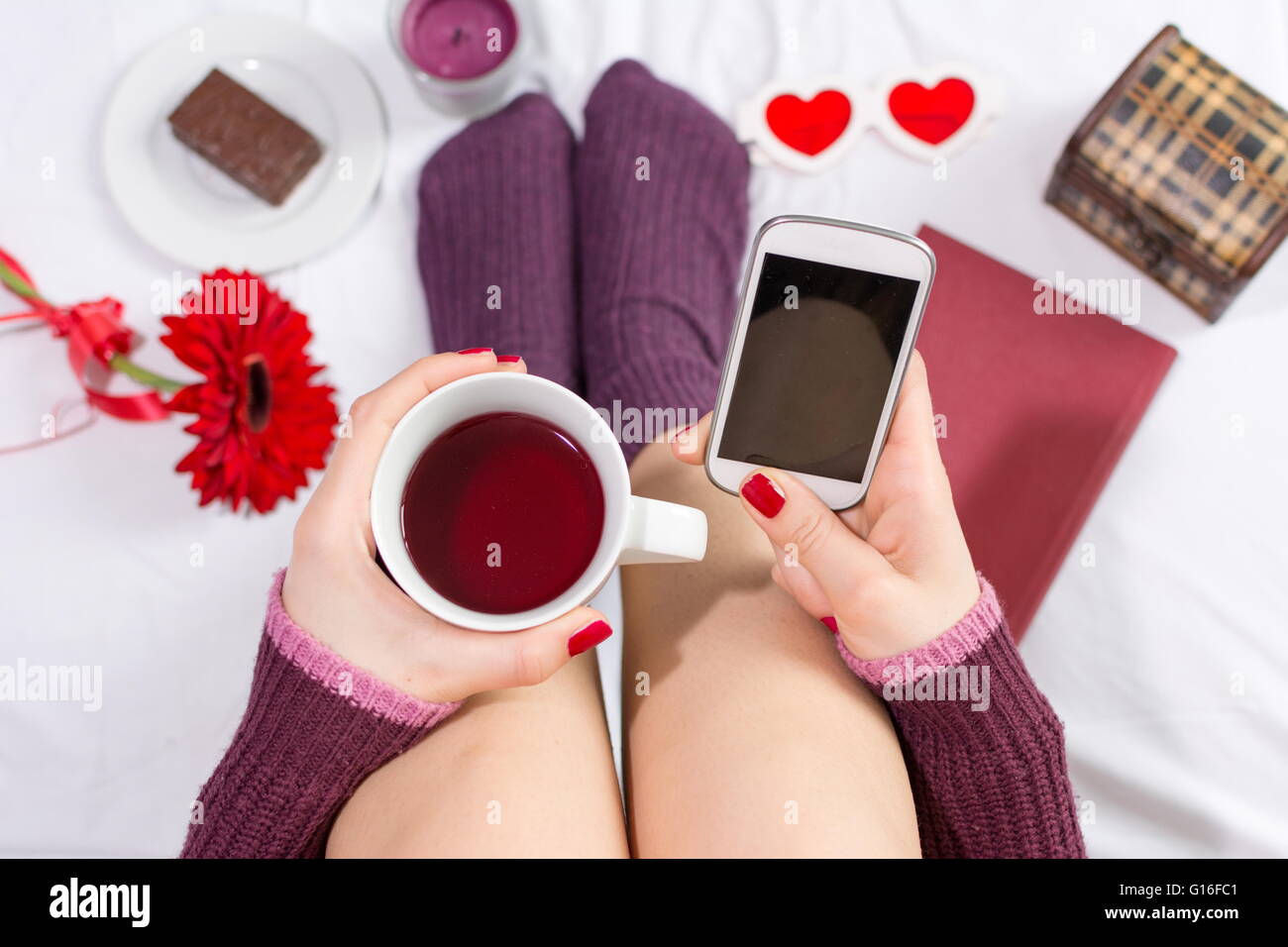 Woman having a cup of tea and texting in bed Stock Photo