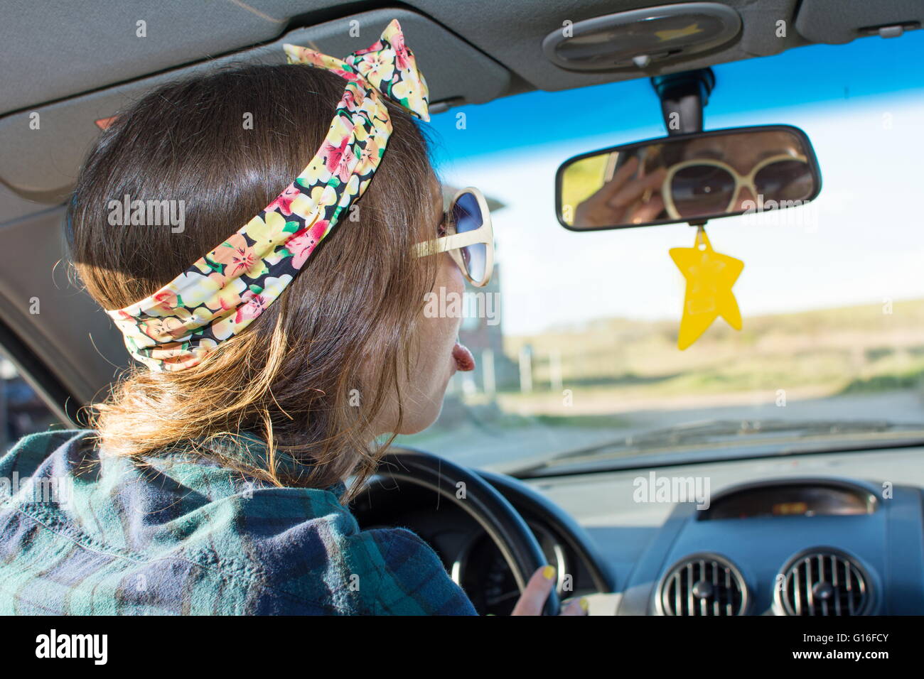 Young woman driving a car and looking herself at the mirror Stock Photo