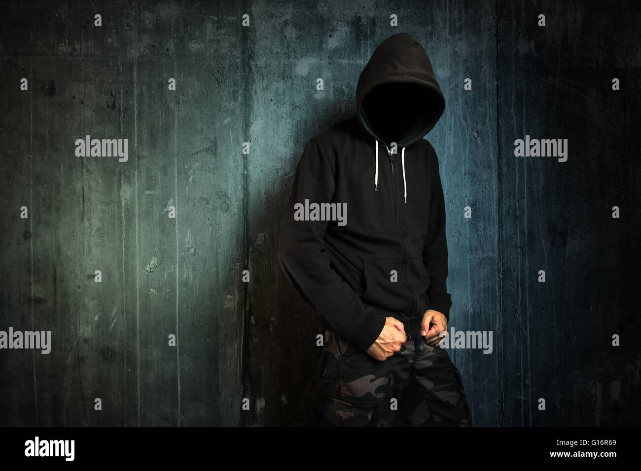 Dangerous unrecognizable faceless criminal standing in front of concrete wall, crime rate and gangster lifestyle concept. Stock Photo