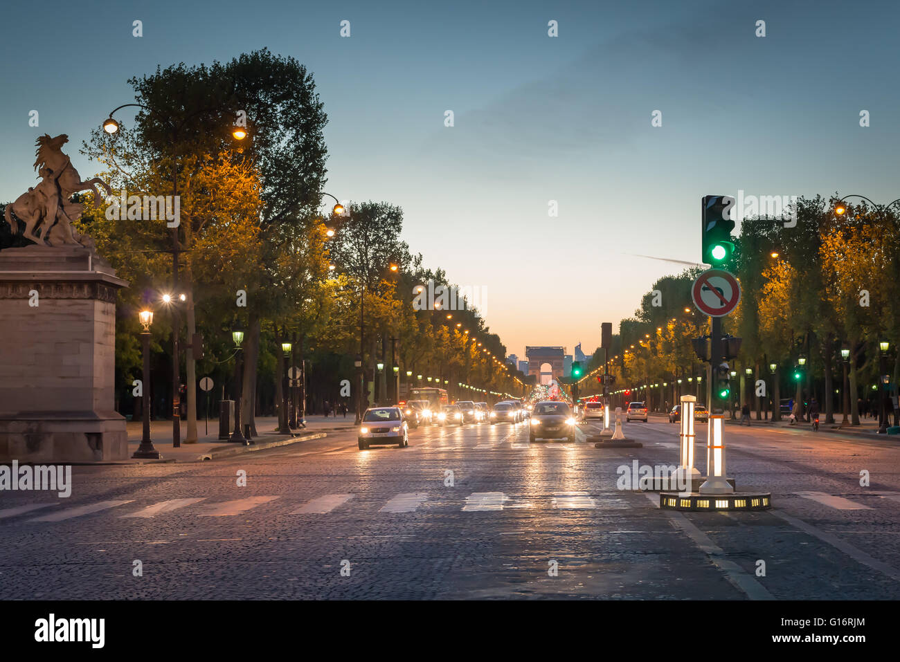 Crossing the Avenue des Champs Elysées with the Arc de Triomphe in the distance, taken at dusk. Traffic on the road approaching pedestrian crossing. Stock Photo