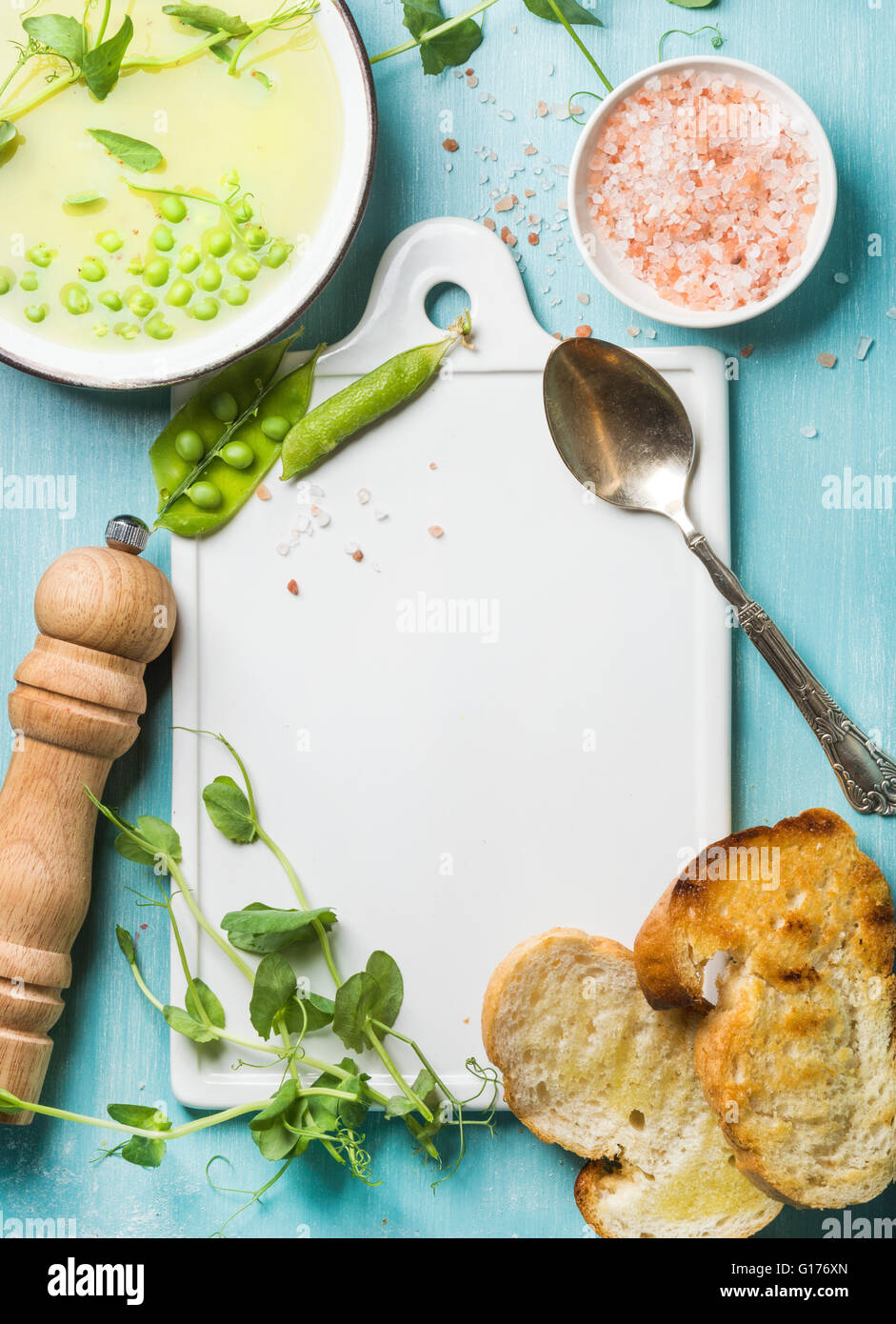 Light summer green pea cream soup in bowl with sprouts, bread toasts and spices. White ceramic board in the center, turquoise bl Stock Photo