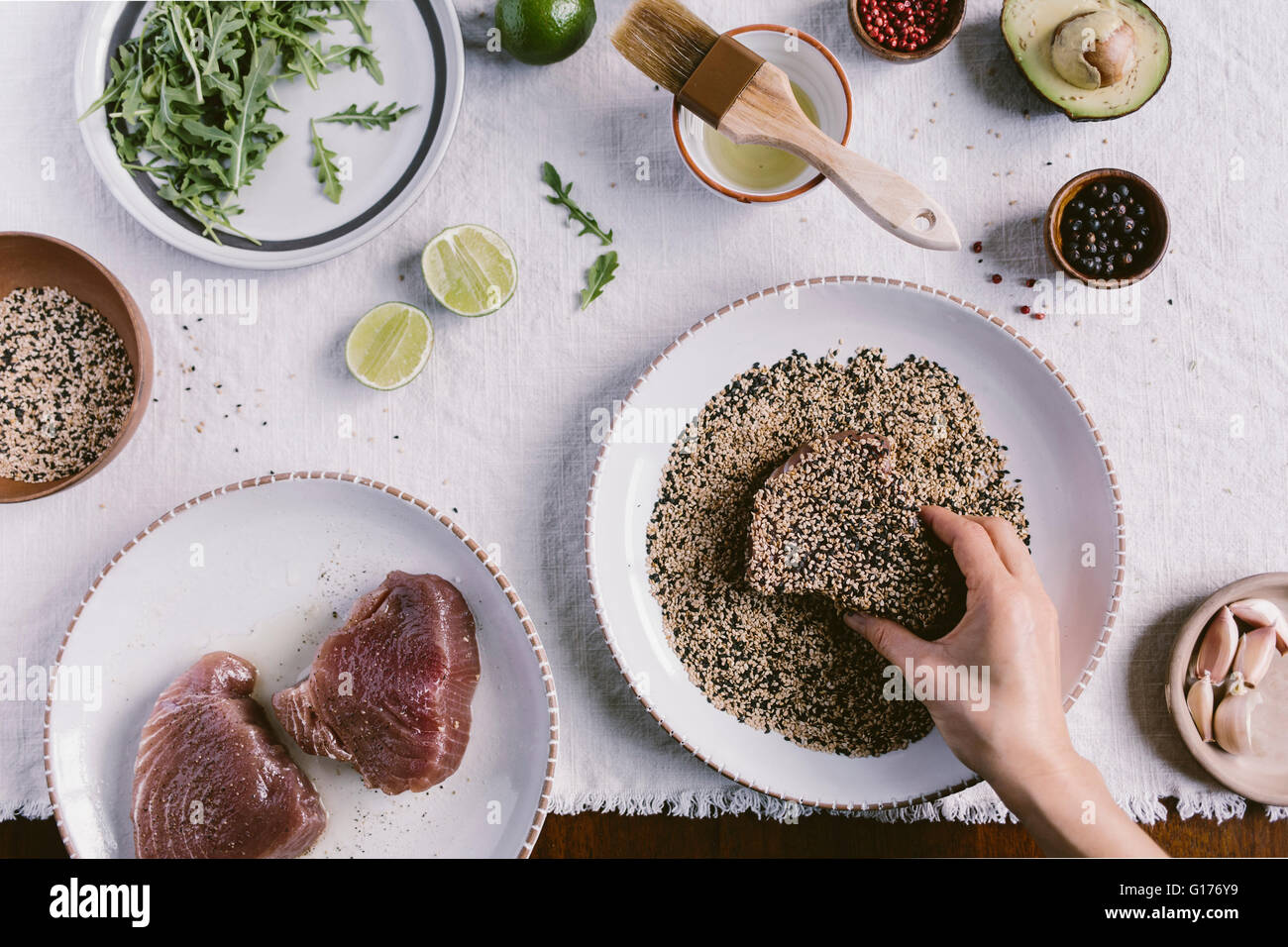 A woman is crusting a piece of yellow fin tuna with black and white