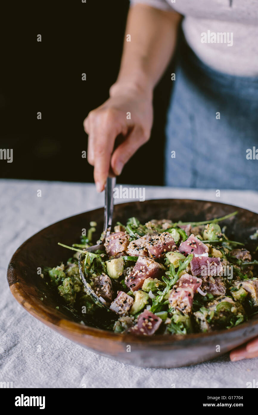 A woman is mixing a bowl of Sesame Crusted Seared Tuna Salad. Stock Photo