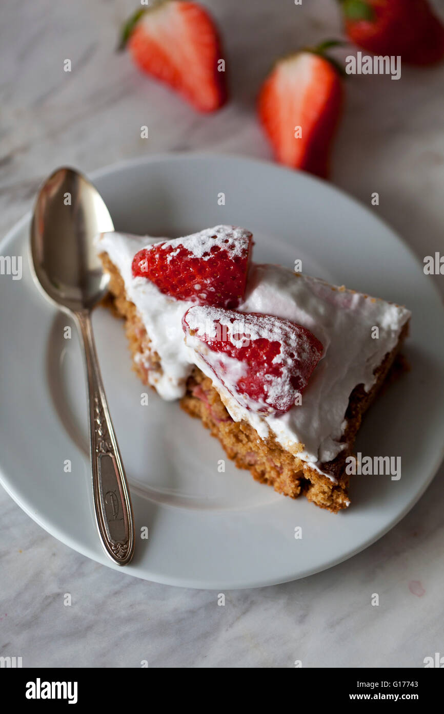 Slice of Strawberry cake with whipped coconut cream and topped with fresh strawberries on a plate Stock Photo