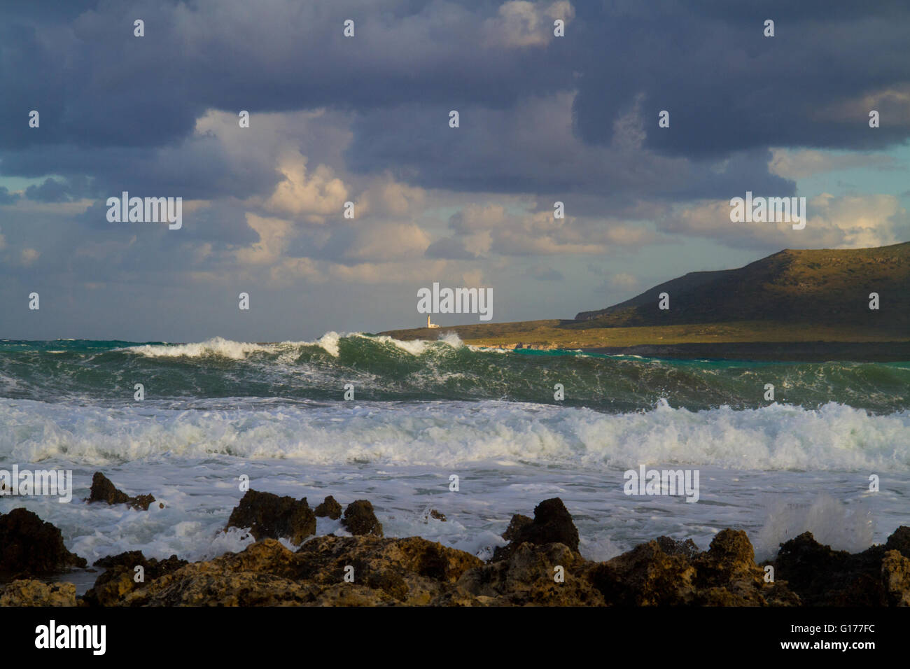 Waves breaking on the rocky shore of the Greek island Kefalonia, in the distance a lighthouse Stock Photo