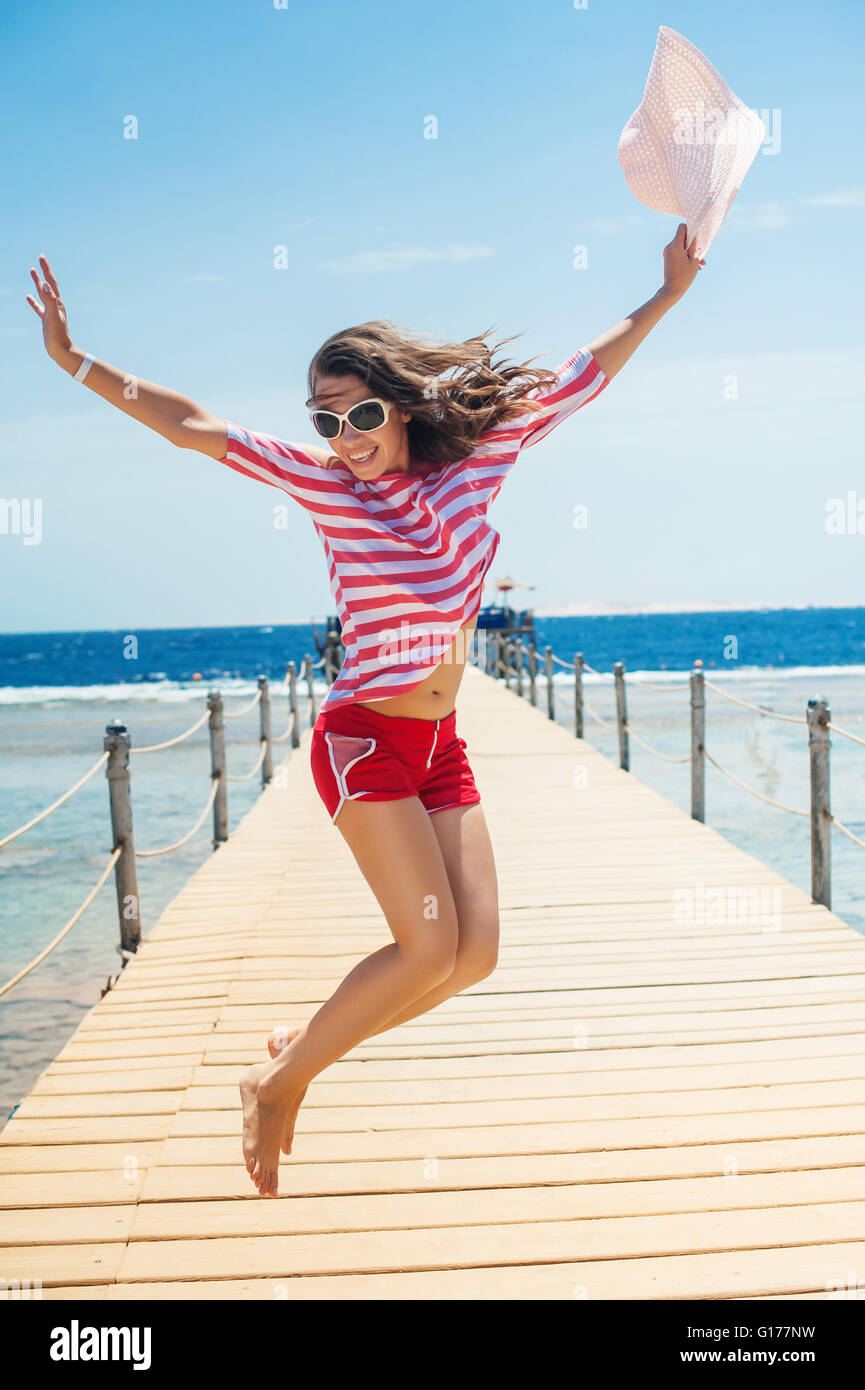 young woman full energy jumping on pontoon in front of sea Stock Photo