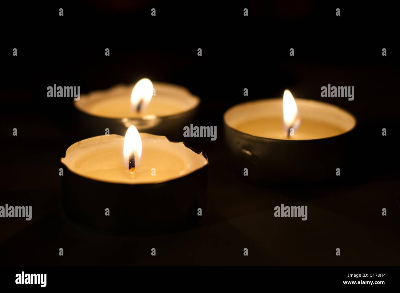 Three burning tea lights on black background. Horizontal image Stock