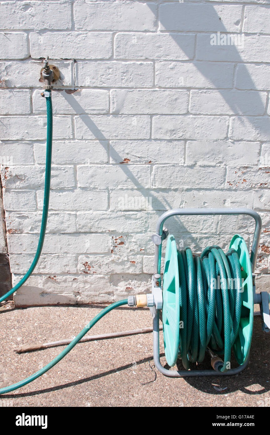hosepipe in the sunny garden next to a bright white wall Stock Photo