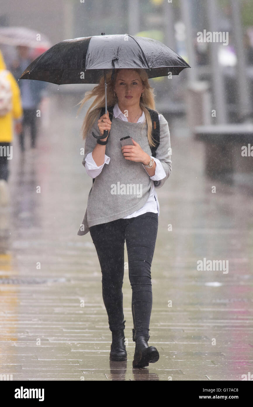 A woman carries an umbrella and mobile phone during heavy rain. Stock Photo
