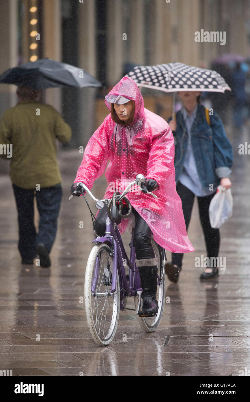 An Asian woman wears a pink poncho while riding a bike during wet weather in Cardiff, Wales. Stock Photo