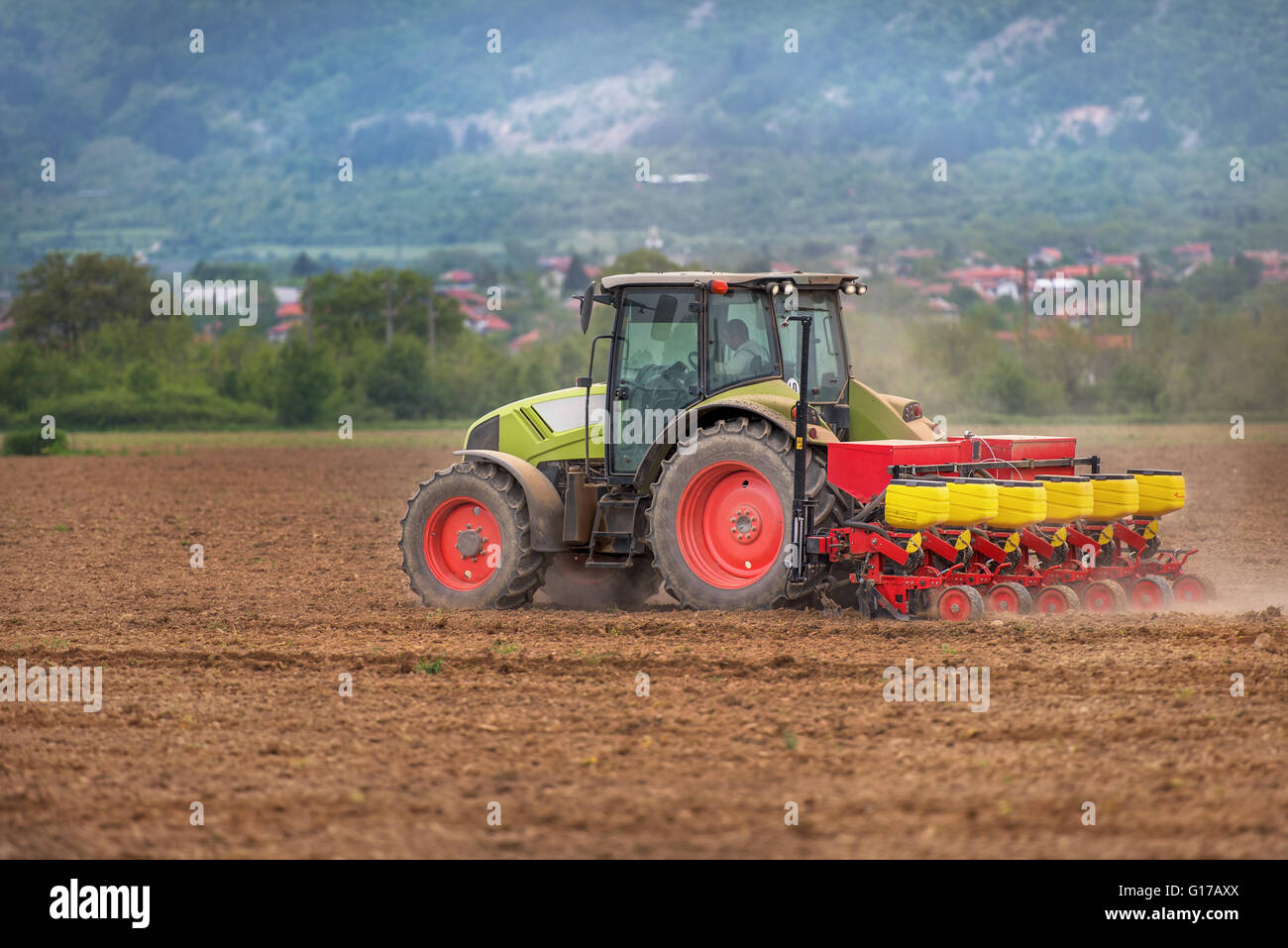 Farmer in tractor sowing crops at field with seed scattering agricultural machine. Stock Photo