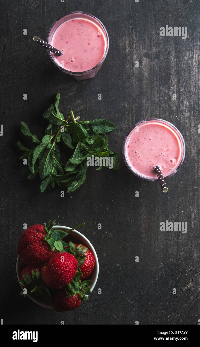 Strawberry and mint smoothie in tall glasses, bawl of fresh berries on dark rustic wood background. Top view, copy space Stock Photo