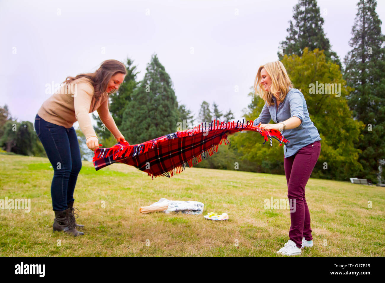 Two young women setting out picnic blanket in park Stock Photo
