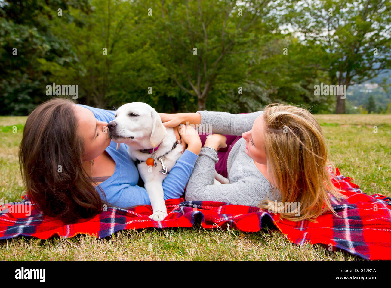 Two young women with pet dog, lying on blanket in park Stock Photo