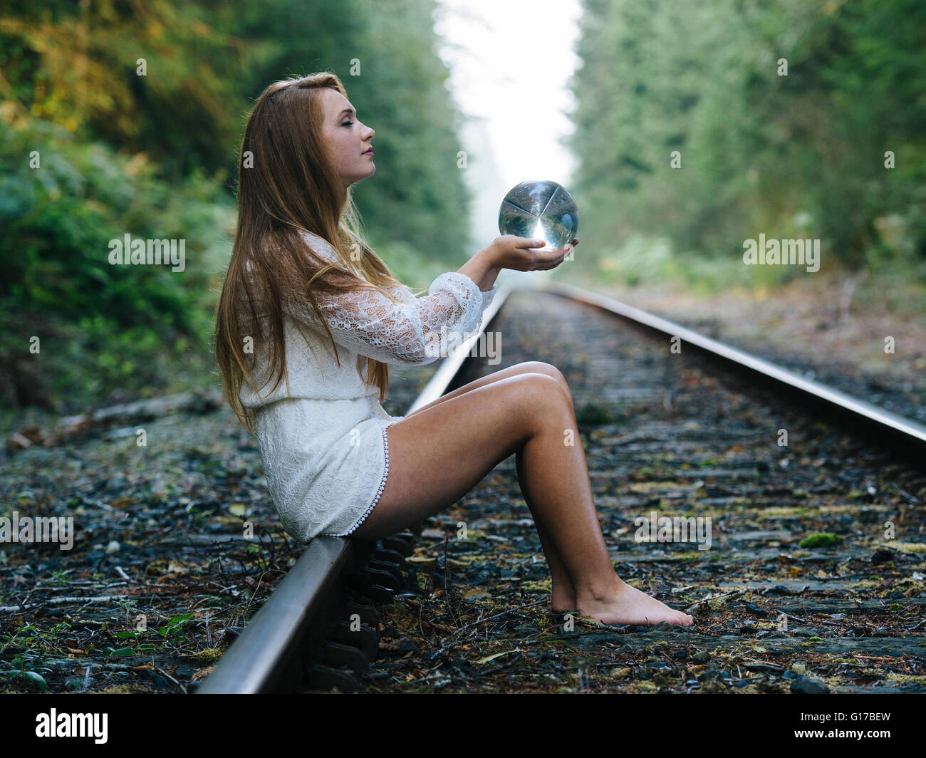 Teenage girl, sitting on train track, holding crystal ball Stock Photo