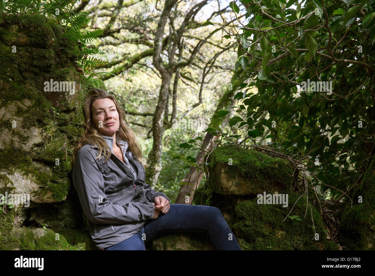 Female hiker sitting on moss covered woodland rocks, Spain Stock Photo