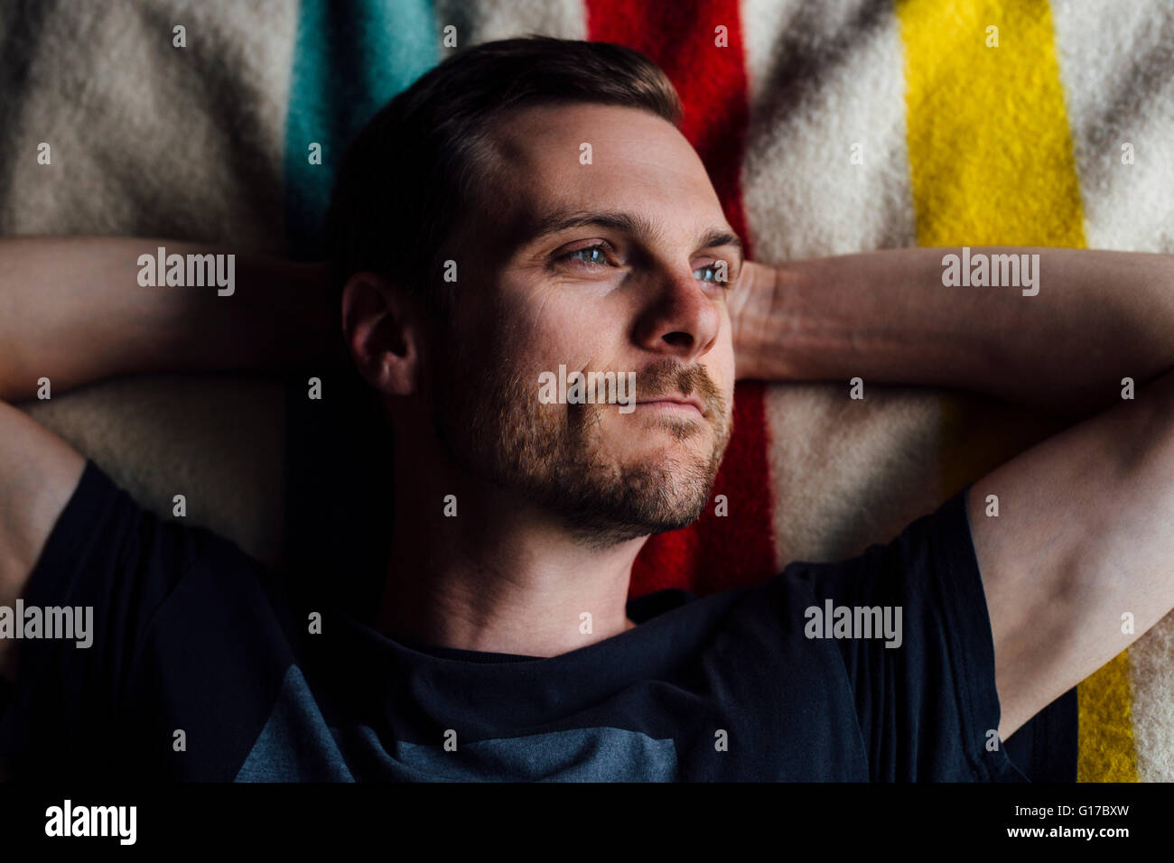 Overhead portrait of handsome man lying on striped blanket with hands