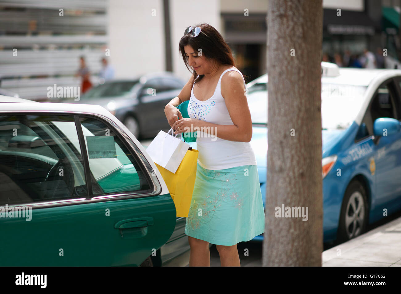 Woman sitting with shopping bags struggling to get into taxi, Los Angeles, California, USA Stock Photo