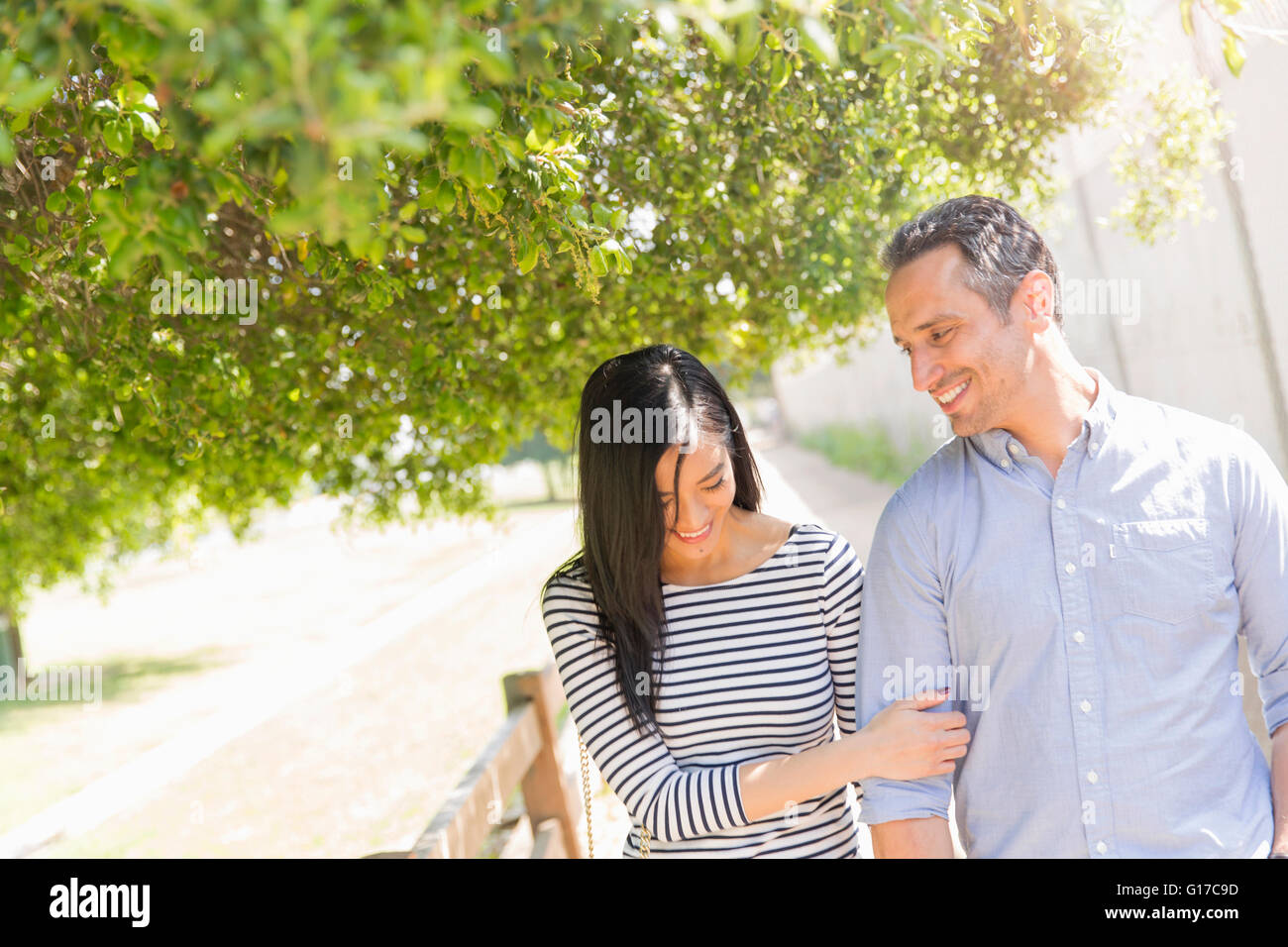 Couple underneath tree linking arms smiling Stock Photo