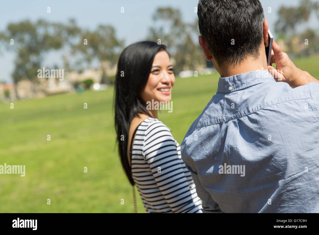 Rear view of couple using smartphone to make telephone call smiling Stock Photo