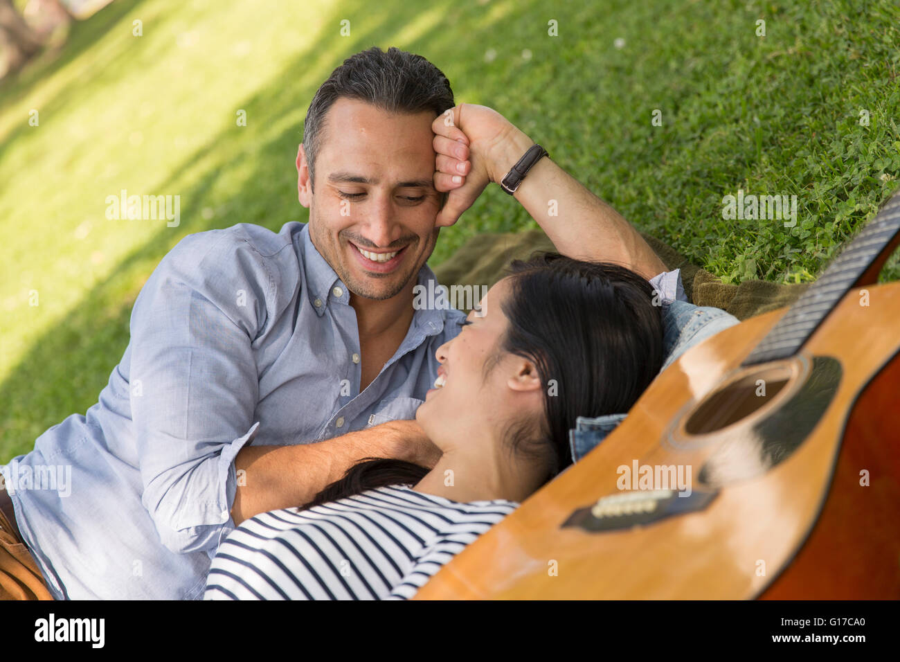 Couple lying on grass with acoustic guitar smiling Stock Photo