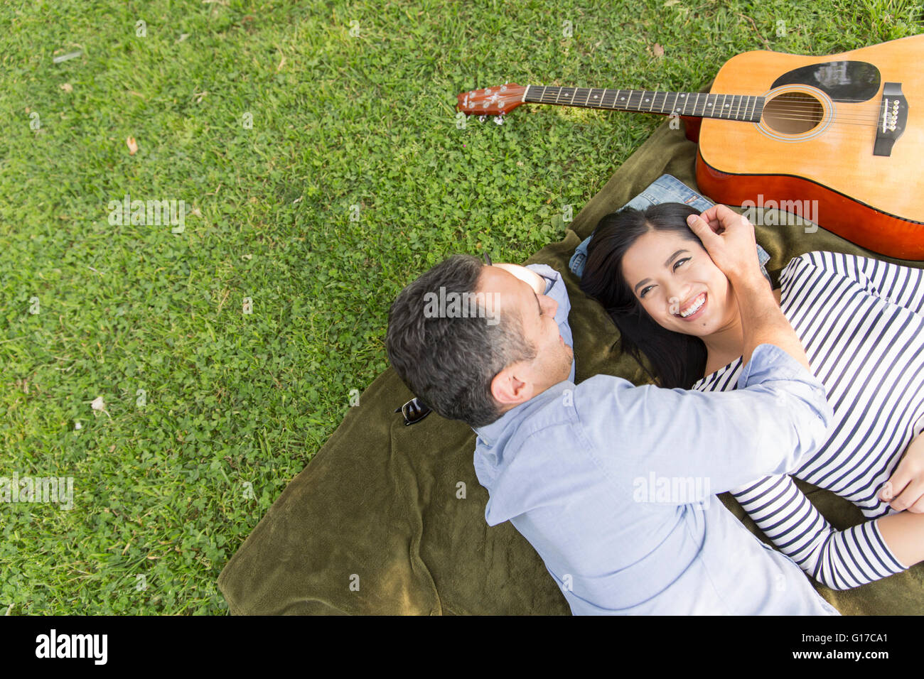 High angle view of couple lying on grass with acoustic guitar smiling Stock Photo