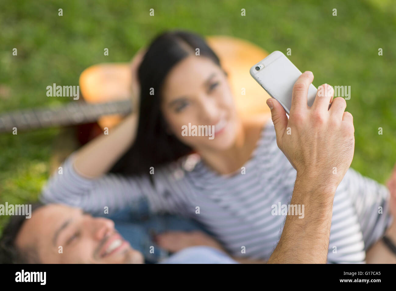 Couple lying on grass using smartphone to take selfie Stock Photo