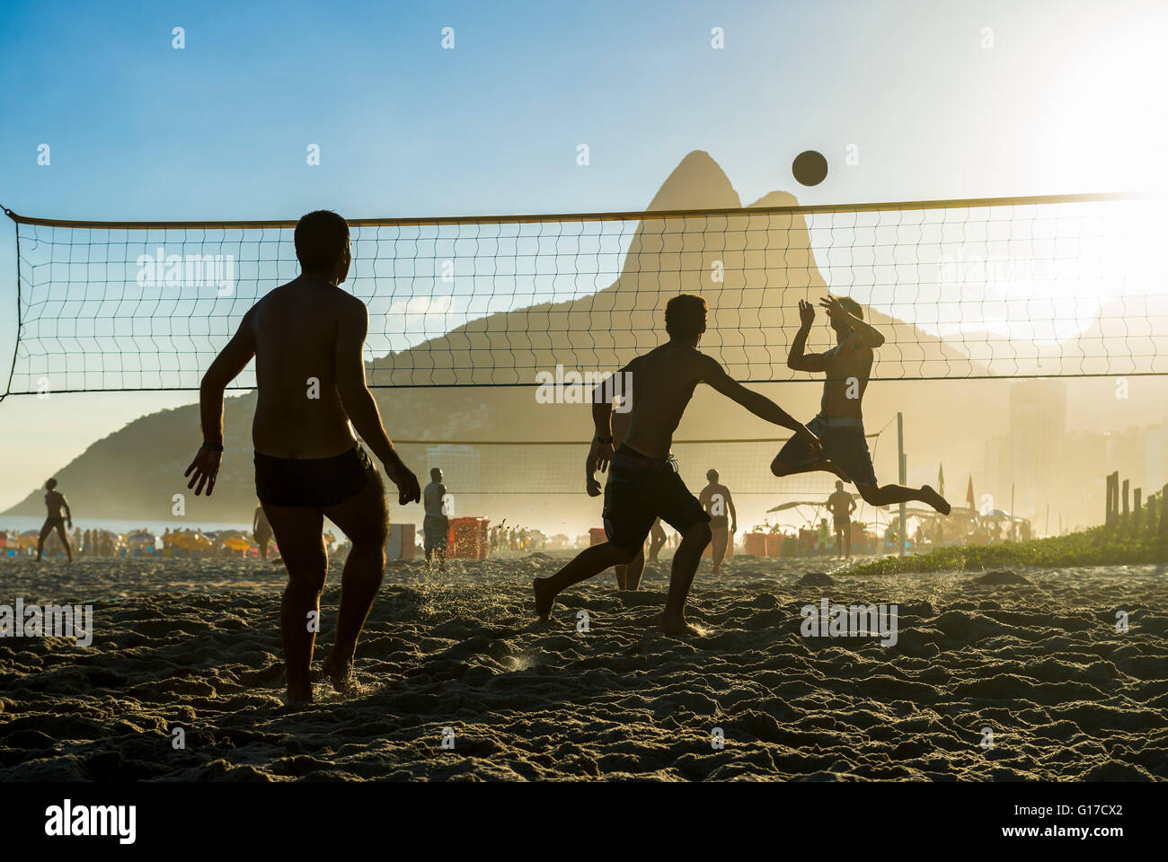 Silhouettes of Brazilians playing futevolei (footvolley) against a sunset on Dois Irmaos Two Brothers Mountain on Ipanema Beach Stock Photo