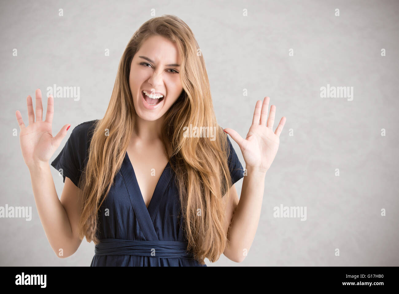 Woman suffering from a nervous breakdown, holding her hands up in the air, isolated in grey Stock Photo