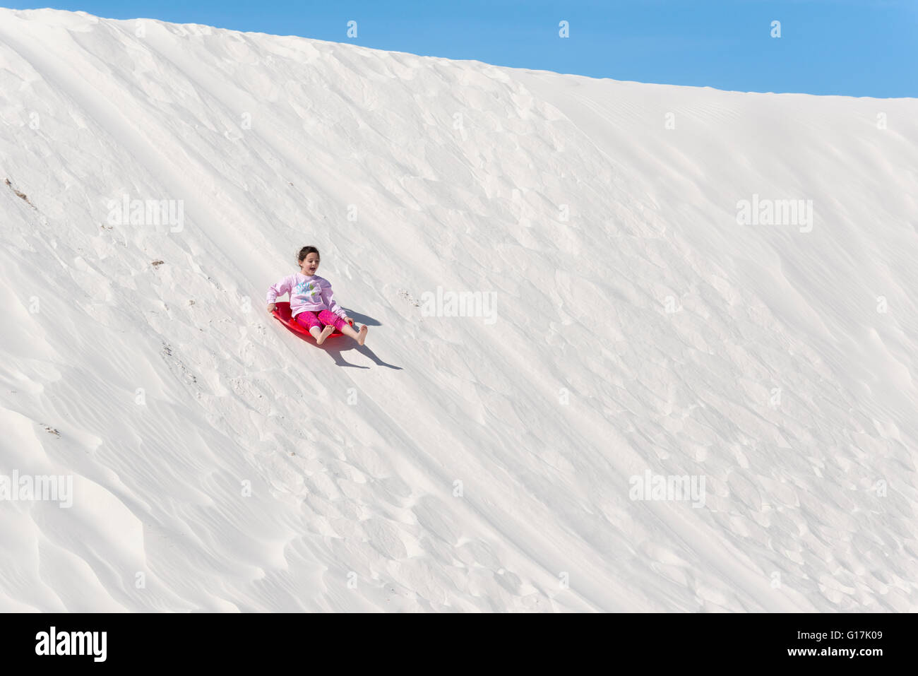 Girl sliding down dune in White Sands National Monument, New Mexico. Stock Photo