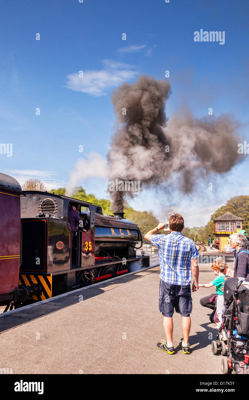 Family watch and take photos at Bolton Abbey Station, as 0-6-0 Austerity Class Saddle Tank Engine blows steam as it leaves the s Stock Photo