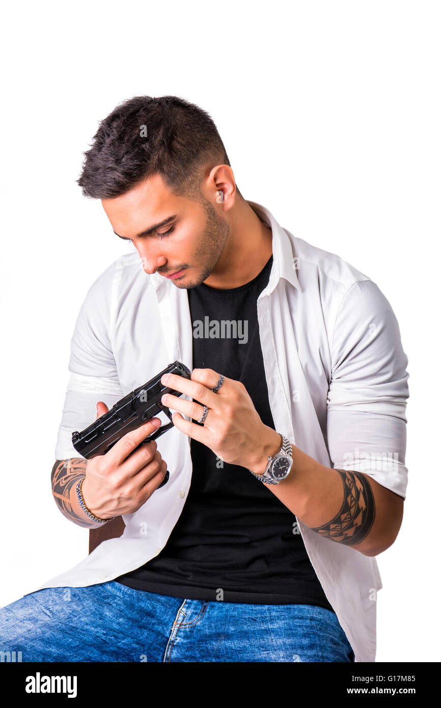 Young handsome man holding a hand gun, wearing black t-shirt, isolated on white background in studio Stock Photo