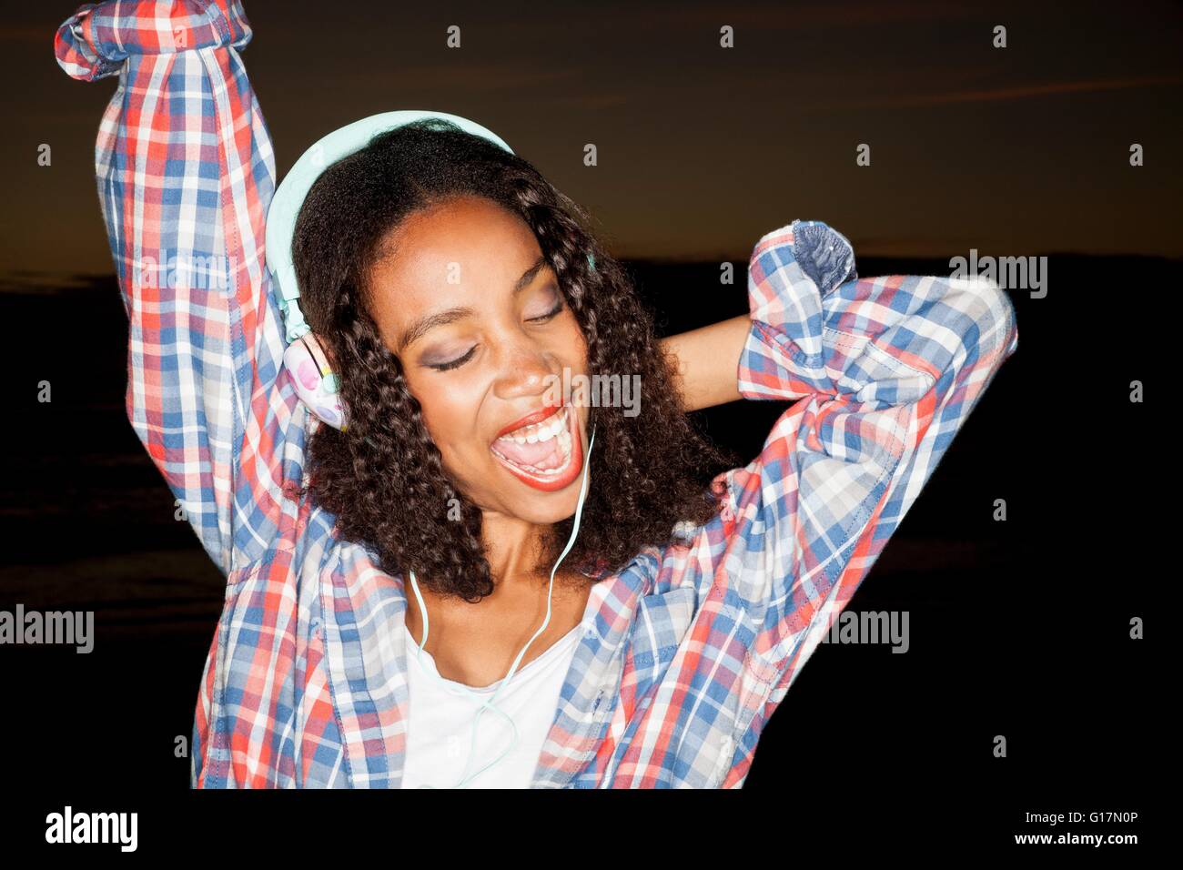 Young woman wearing headphones arm raised, eyes closed open mouthed smiling Stock Photo