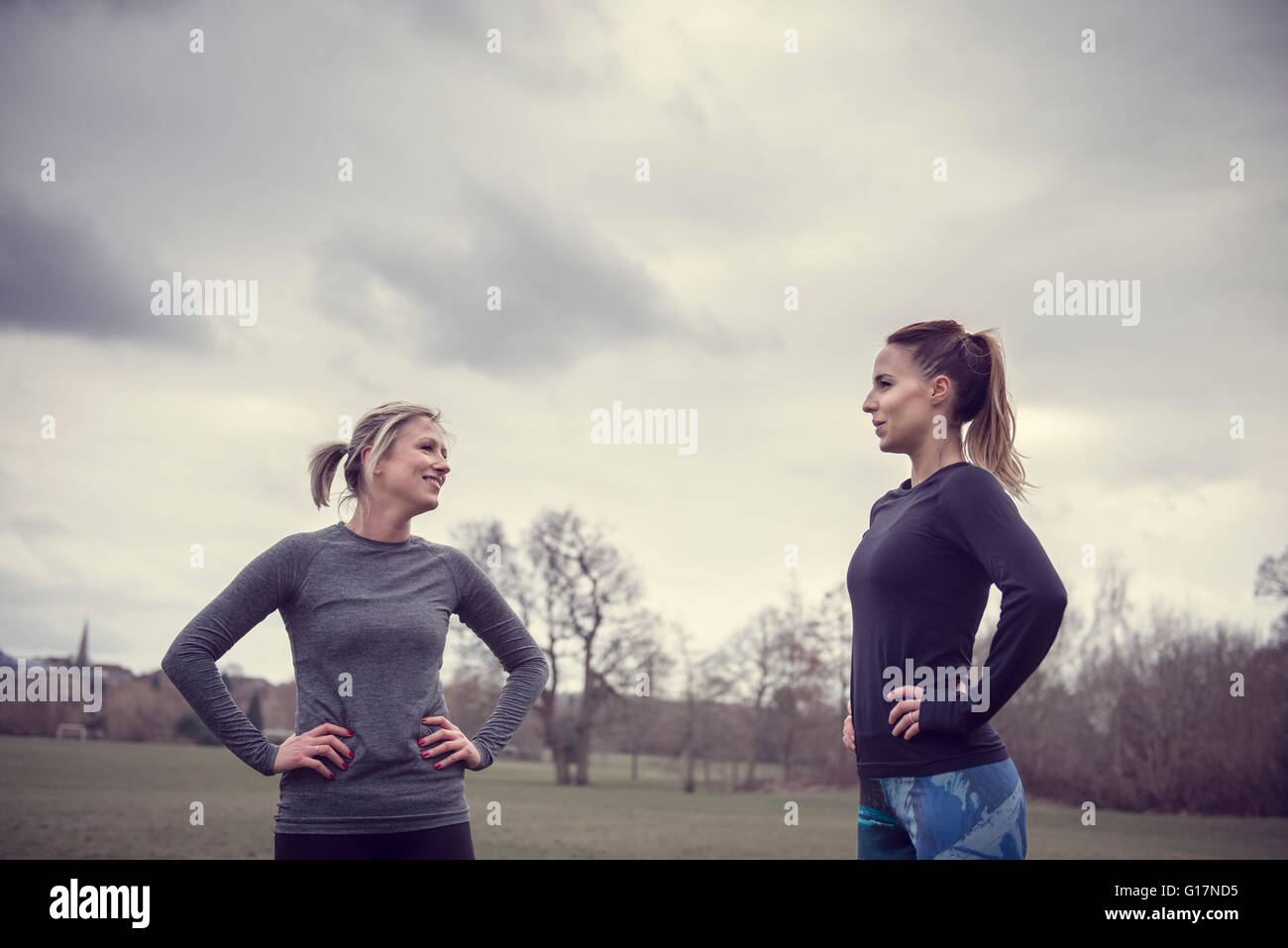 Women wearing sports clothes in field hands on hips face to face smiling Stock Photo