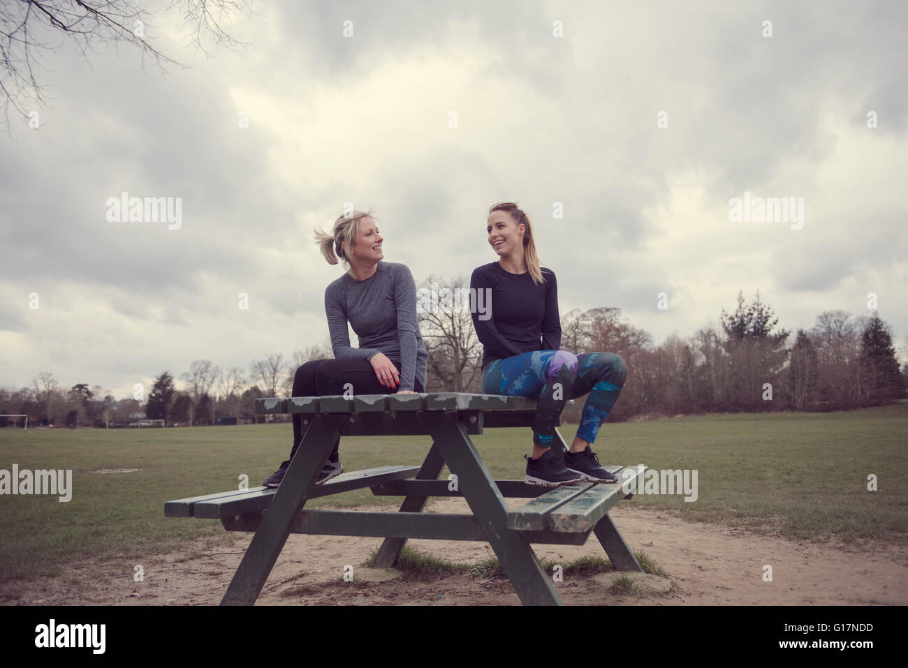 Women wearing sports clothing sitting on picnic table chatting Stock Photo