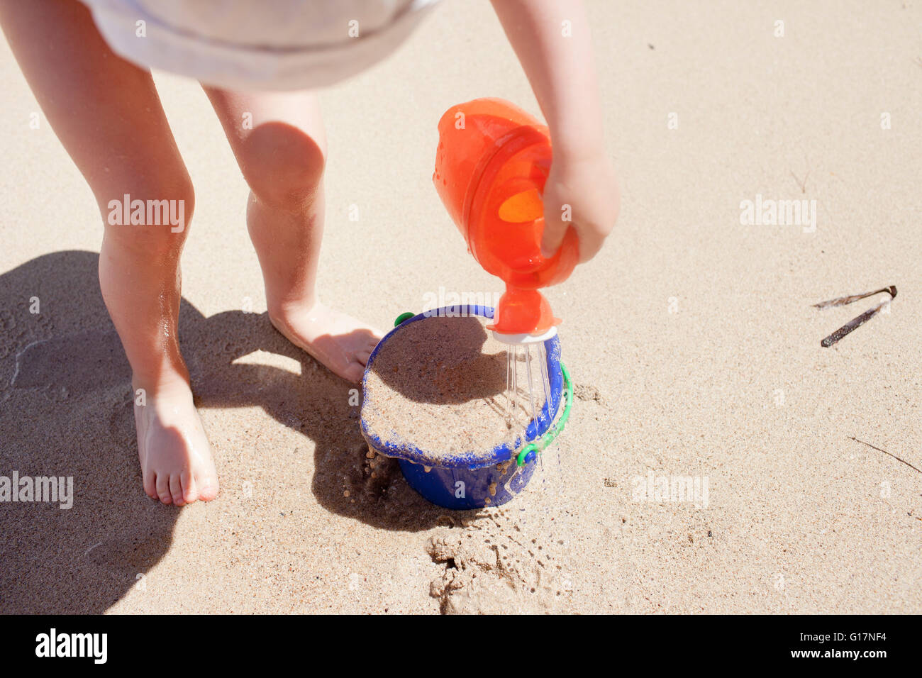 Baby girl pouring water on bucket of sand, elevated view Stock Photo