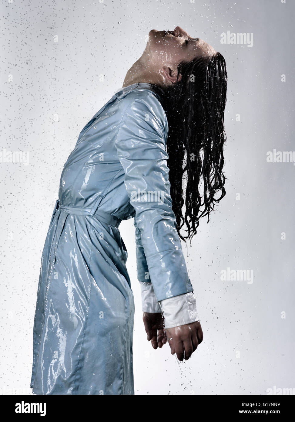 Side view of woman wearing raincoat drenched in water throwing back head Stock Photo